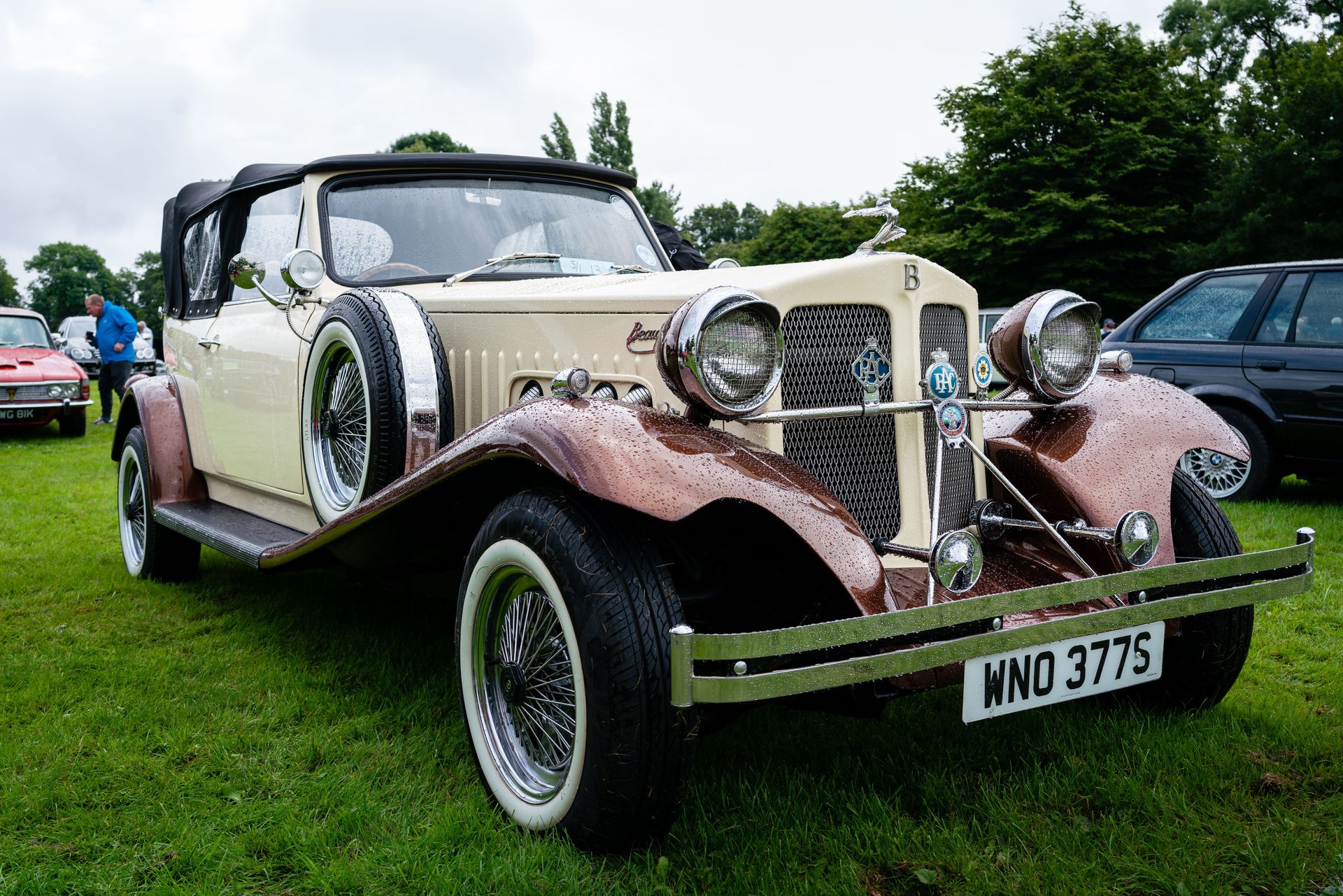 Vintage Beauford parked on a grass field with raindrops, exuding timeless elegance.